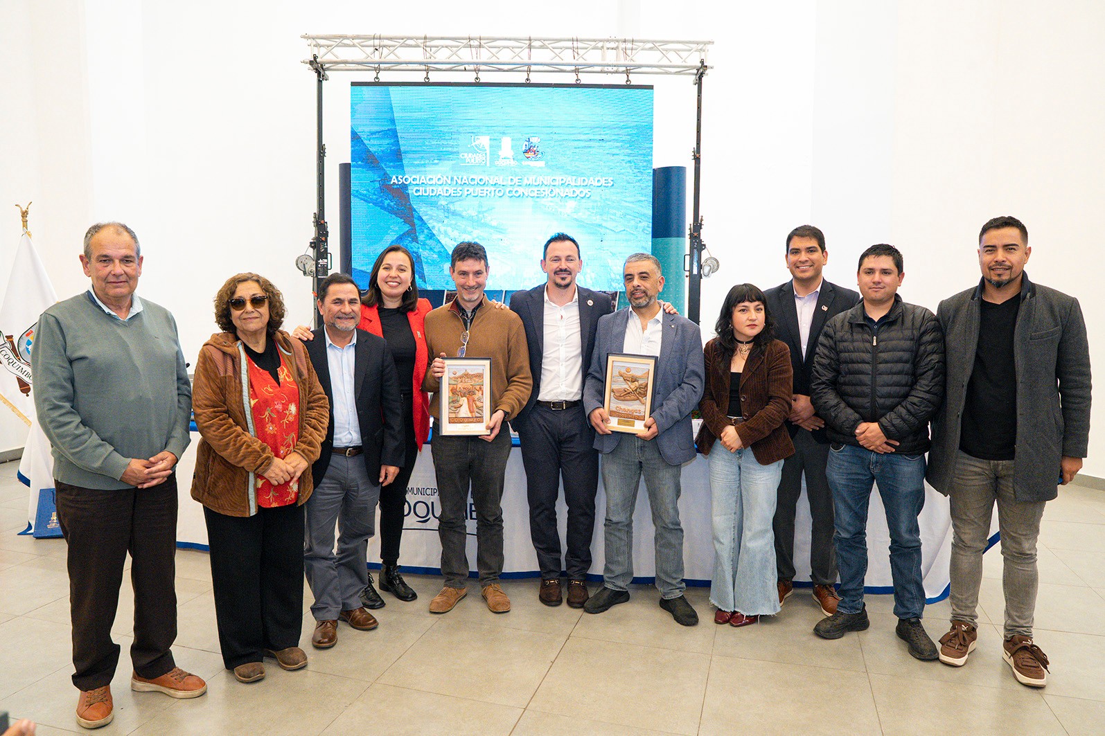 Autoridades posan con dos reconocimientos enmarcados tras la asamblea de la ANCPCH en Coquimbo